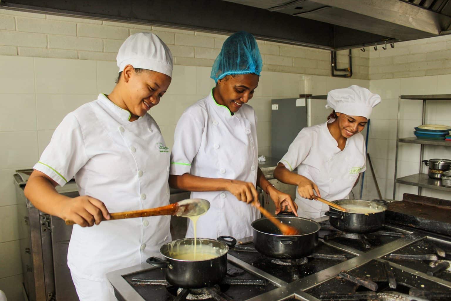 Tres mujeres en una cocina cada una haciendo su plato de comida frecemos oportunidades de inversión que se centran en el desarrollo sostenible y la generación de un triple impacto duradero.