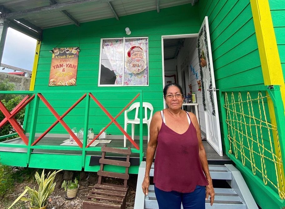 Una mujer mostrando el frente de su hogar ,Nuestro enfoque en el impacto económico e impacto ambiental busca impulsar la prosperidad local y fortalecer la resiliencia comunitaria