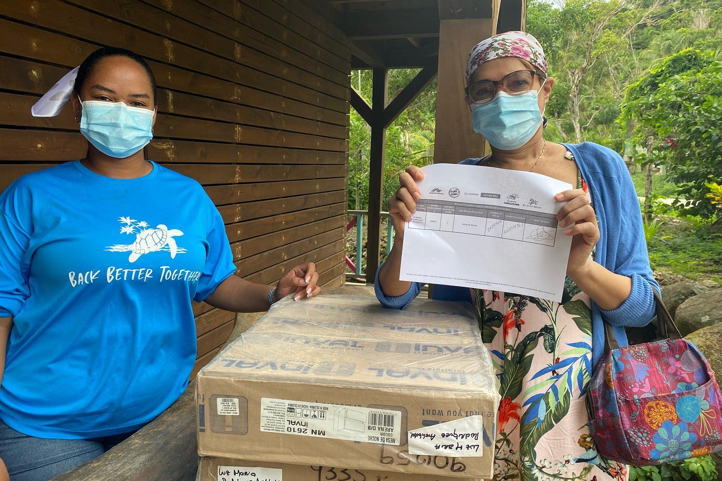 Dos mujeres con tapaboca una de ellas muestra una clase de certificado de entrega de ayuda ,Nuestros esfuerzos en Desarrollo Sostenible se traducen en iniciativas transformadoras que tienen un alto impacto en la comunidad y el entorno