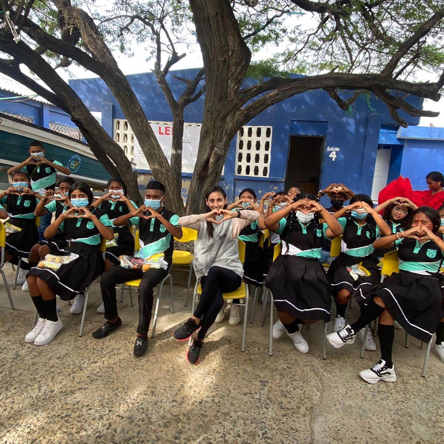 Estudiantes junto a su maestra agradeciendo el compromiso one inversión colocando sus manos en forma de corazón ,El cambio hacia una ecolonomía social es esencial para lograr un impacto comprobado y un futuro mejor.