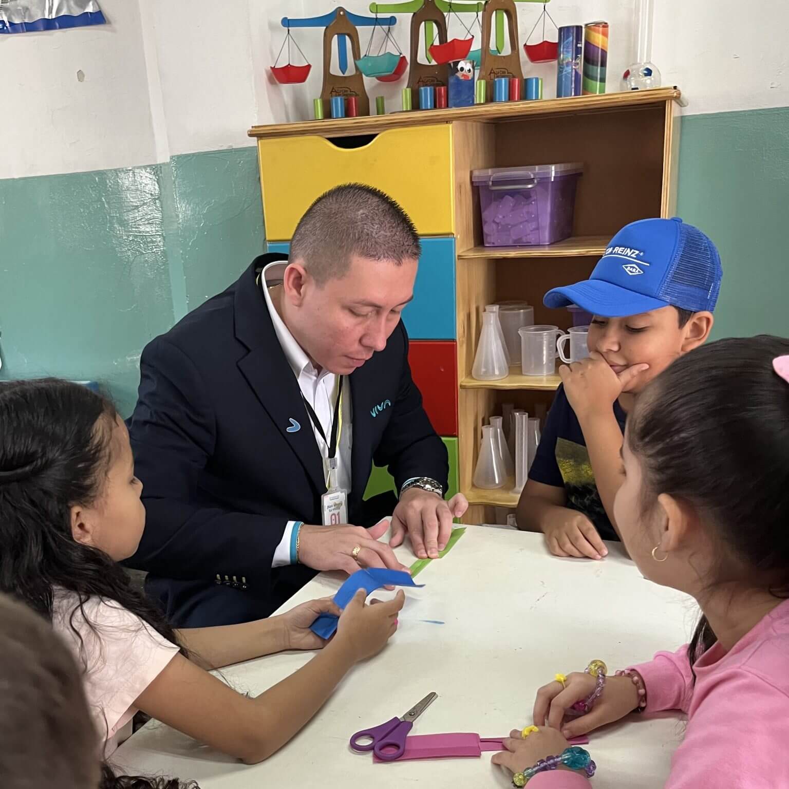 Profesor sentado con sus alumnos en clases y mostrandoles como realizar su tarea con el material El Desarrollo Sostenible guía nuestras acciones, enfocándonos en crear un impacto social significativo y alto impacto en la calidad de vida