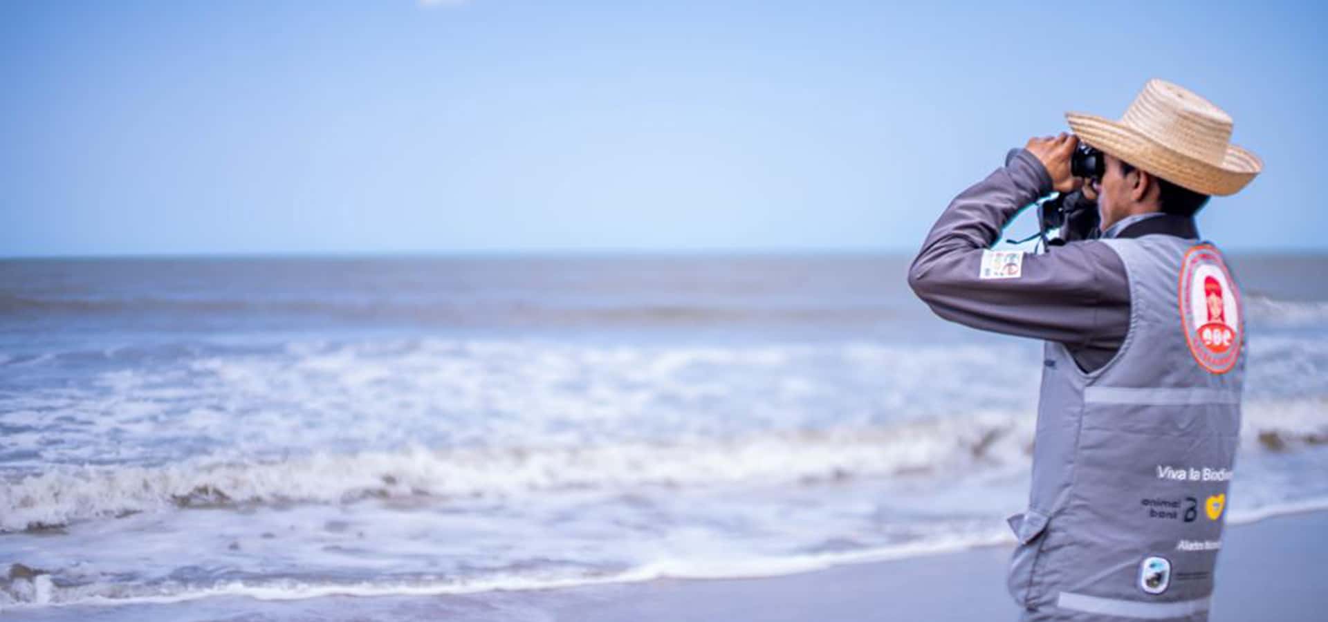 Hombre mirando por binóculos hacía el horizonte y el mar El verdadero impacto social se logra cuando las comunidades se empoderan y participan activamente en las soluciones.