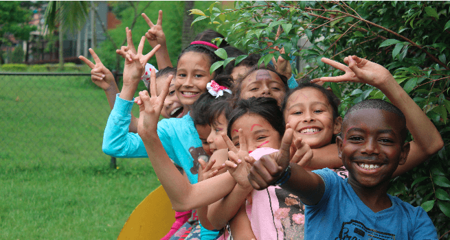 Grupo de niño haciendo fila y sonriendo ,creemos en la inversión social como herramienta para lograr un impacto social y ambiental positivo.