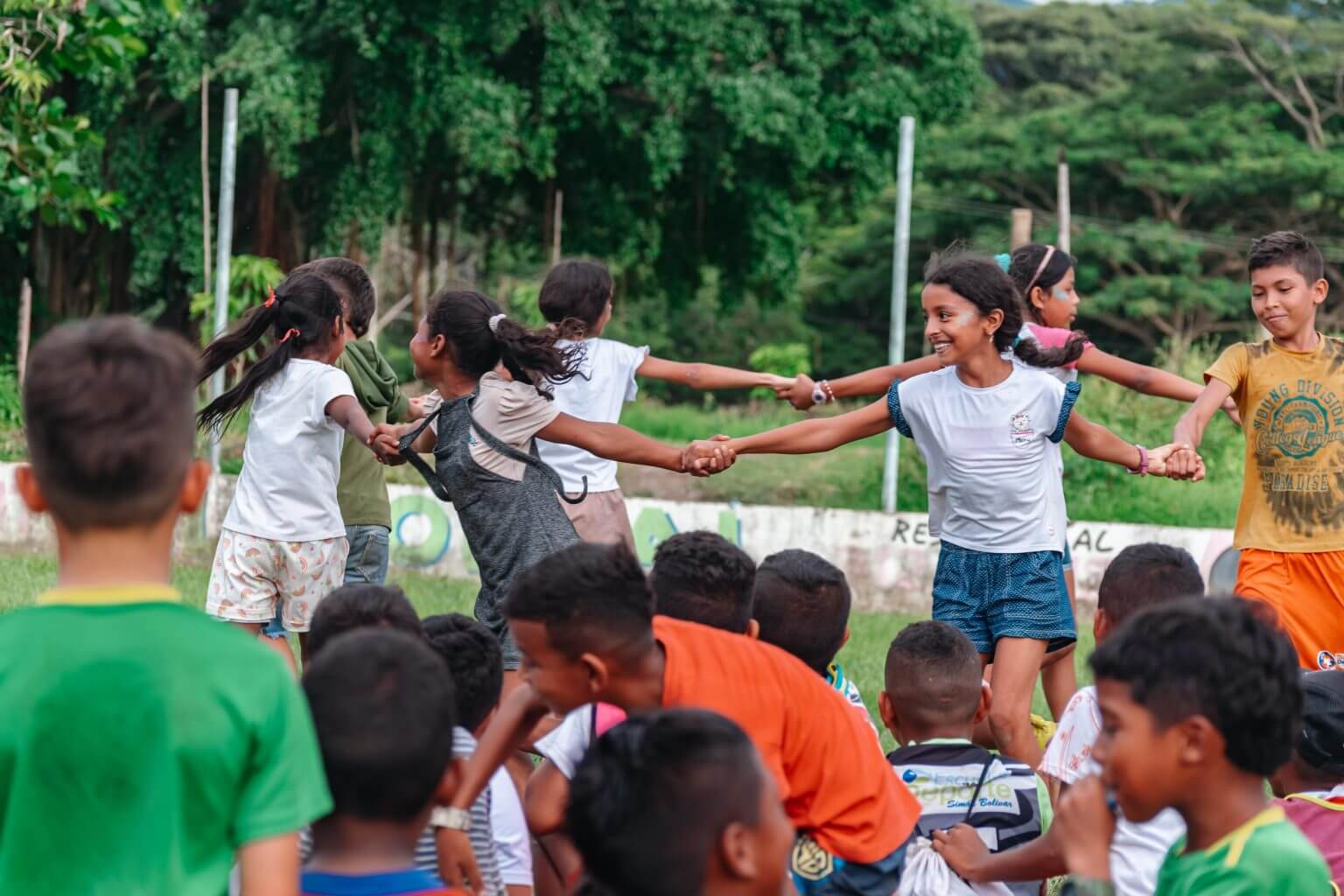 Children playing, holding hands and spinning outdoors. Our strategic alliances enhance our social business model, ensuring economic growth and sustainable development.