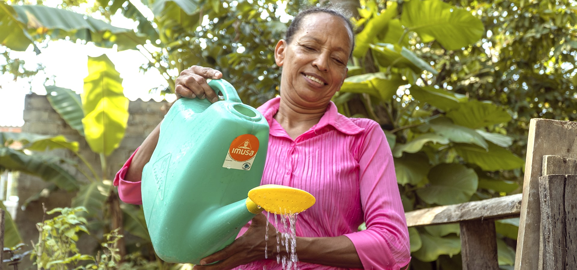 A woman smiling while watering her plants, emphasizing the environmental strategies that ONE Social Investment employs as high-impact initiatives.