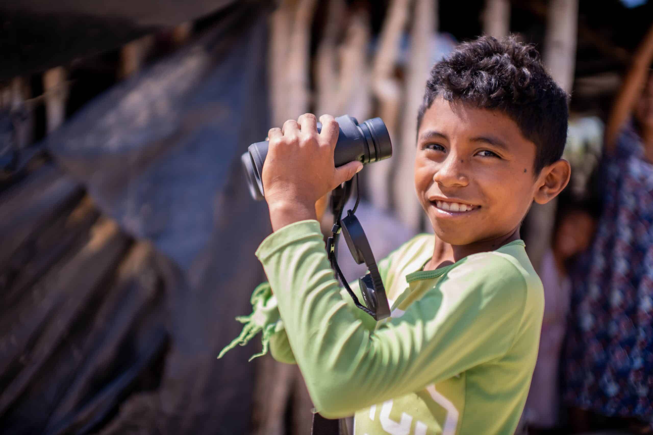 Un niño sonriendo y en sus manos unos binóculos, El compromiso con el impacto social exige una visión a largo plazo y una dedicación inquebrantable al bienestar comunitario.
