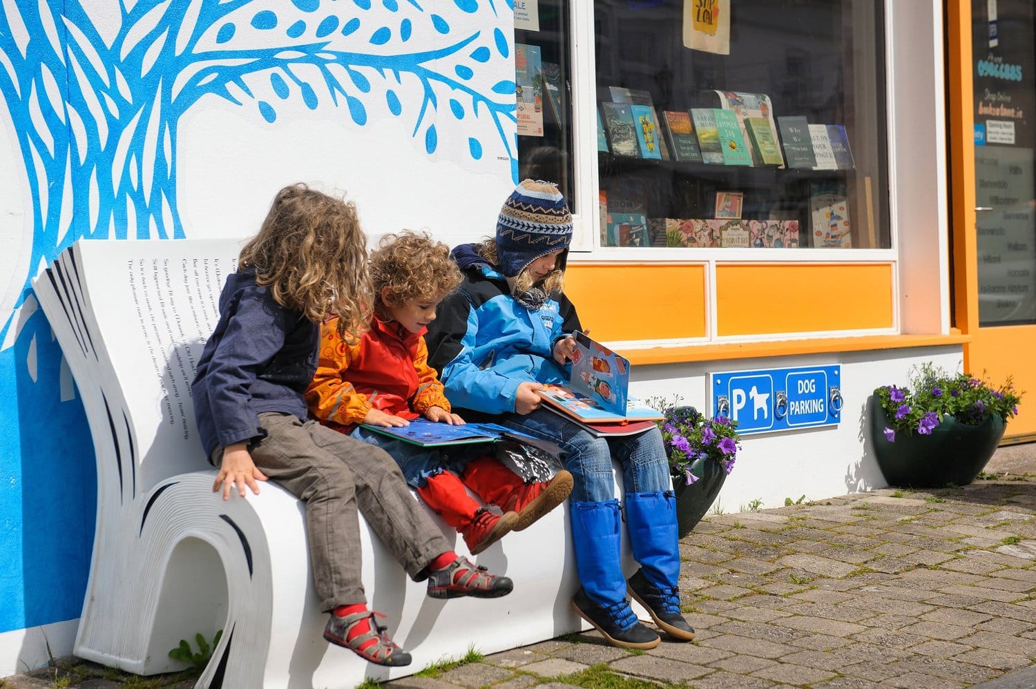 Tres niños leyendo afuera de una librería comunitaria gracias a sus aportes en nosotros y ayudándonos a construir un futuro mejor de Impacto social.